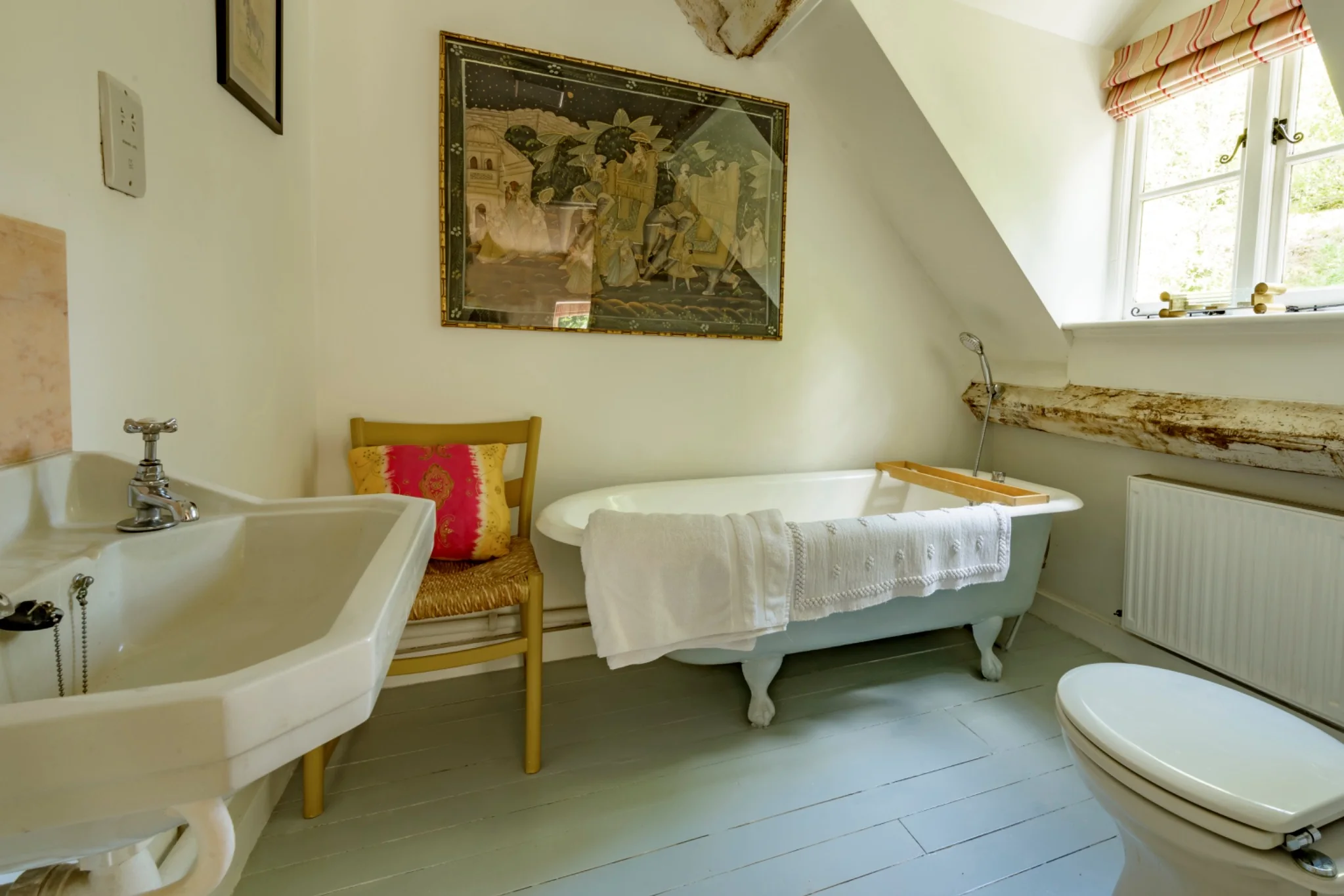 Bedroom one’s en-suite bathroom with a roll-top bath, pink cushion and large picture